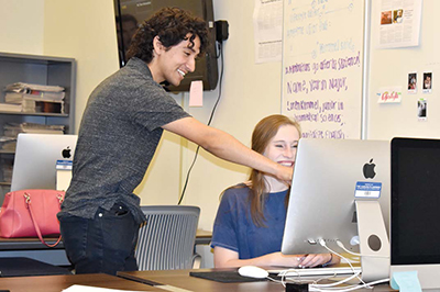 Man points at computer screen over girls shoulder.