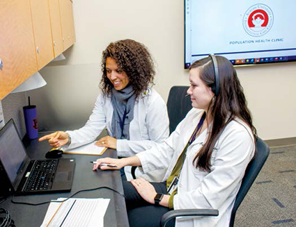 Two women in white coats sit at computer