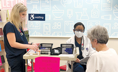 Two pharmacists wearing masks sit and speak with patient