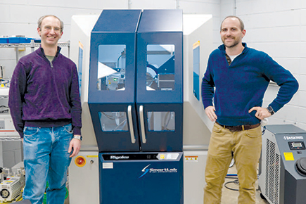 Two men stand on either side of blue x-ray machine