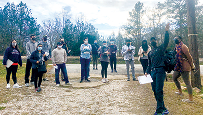 Group of students stands outside looking up at tree that teacher is pointing to