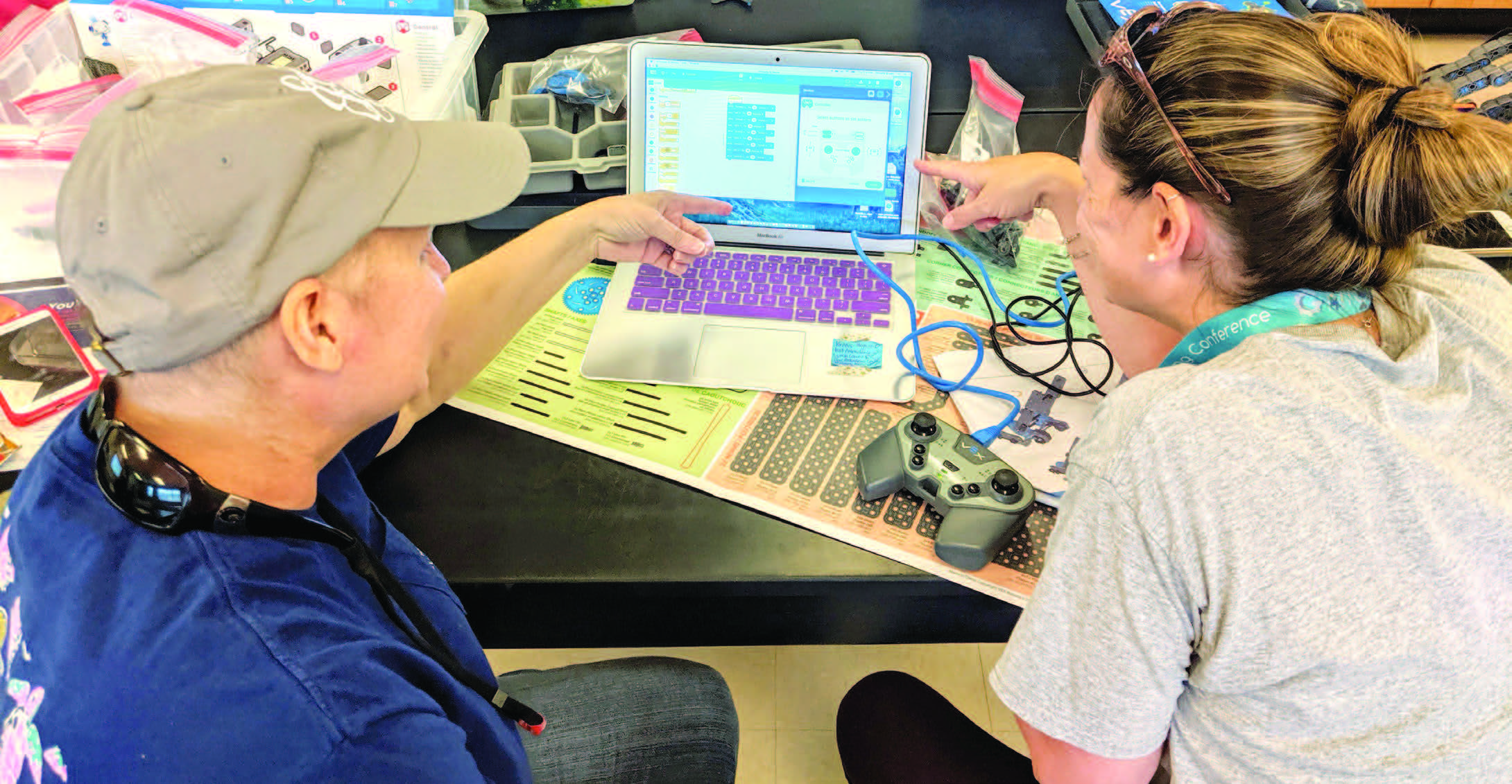 Man and woman sit at laptop pointing at screen.