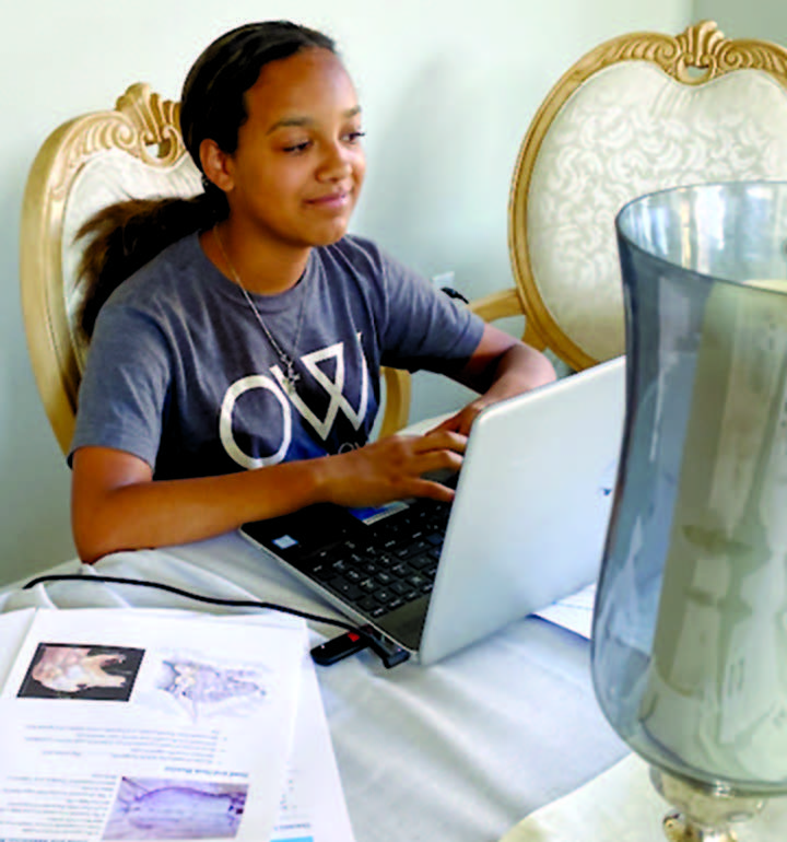 School-aged girl sits at tablet working on laptop