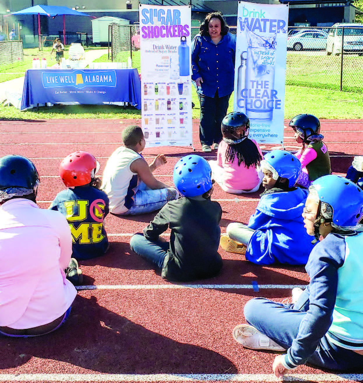 Woman stands next to banners in front of school kids sitting on ground