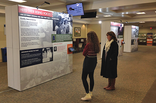 Two women stand and look at Alabama Justice exhibit by Steven Brown