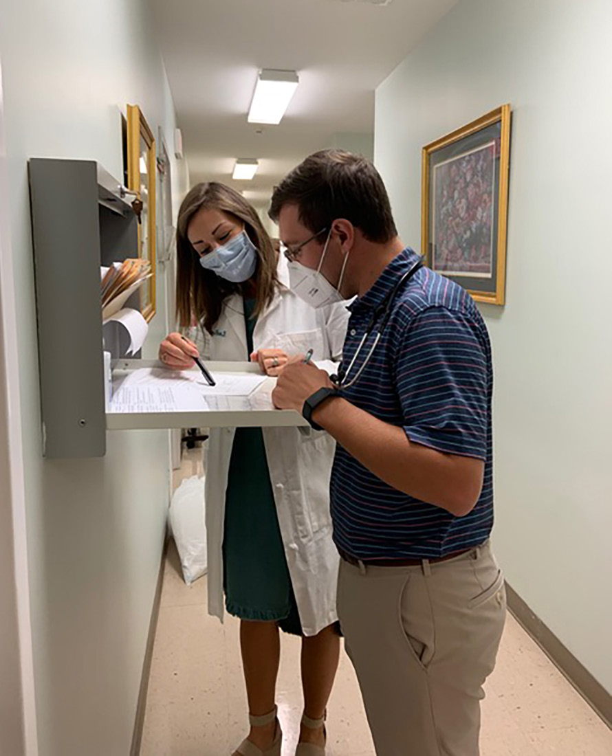 Nurse in white coat points out something in file to man while standing at filing cabinet